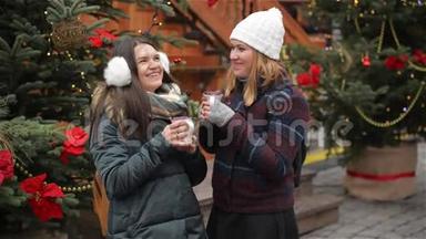 两个漂亮的女朋友在圣诞市场上谈笑风生。 朋友畅饮热饮，享受欢乐